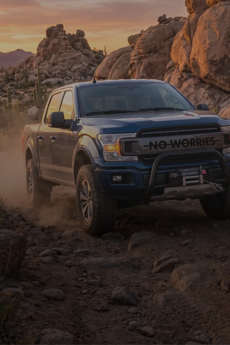 Blue pickup truck driving on a desert trail at sunset